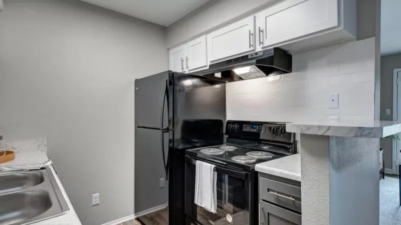 A bright kitchen featuring white cabinets, with a countertop, sink, gas stove, microwave oven, and other appliances. The walls are adorned with cabinetry and there is a floor beneath.
