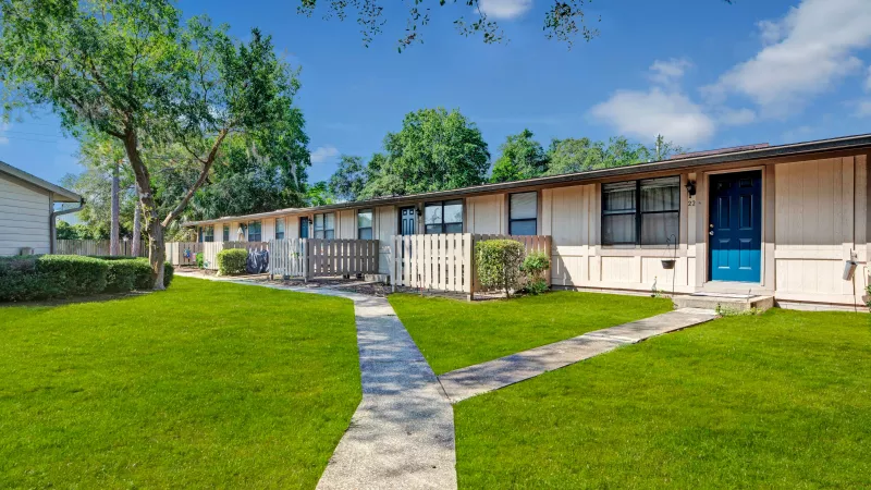 A Y-shaped concrete pathway leading to single-story residential units with green lawns and large trees.
