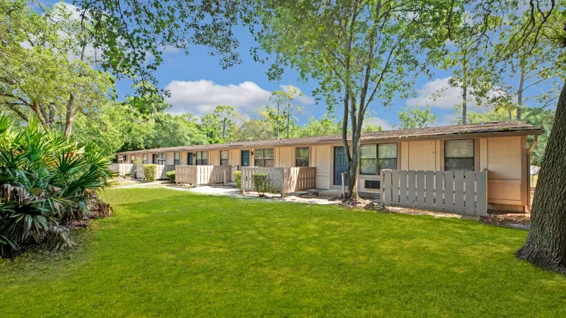 A scenic view of beige apartments amidst lush trees and open green spaces, showcasing a quiet residential atmosphere.