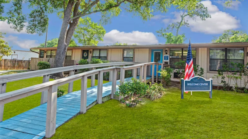 The front facade of the "Welcome Center" building, with a blue door and a ramp flanked by lush greenery.
