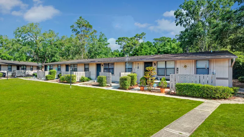 A row of beige residential units with neatly landscaped gardens and a concrete pathway.