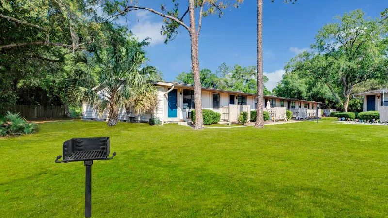 A green lawn with a barbecue grill in the foreground and a row of residential units in the background.