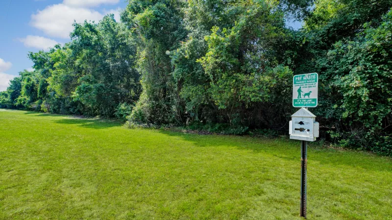 A close-up of a pet waste station surrounded by green grass and trees.