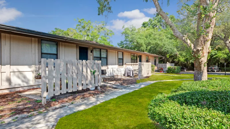 A residential unit with a small patio area, surrounded by a lush green lawn and landscaping.
