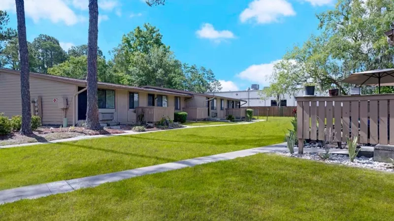A green courtyard with single-story apartment units and a walking path.