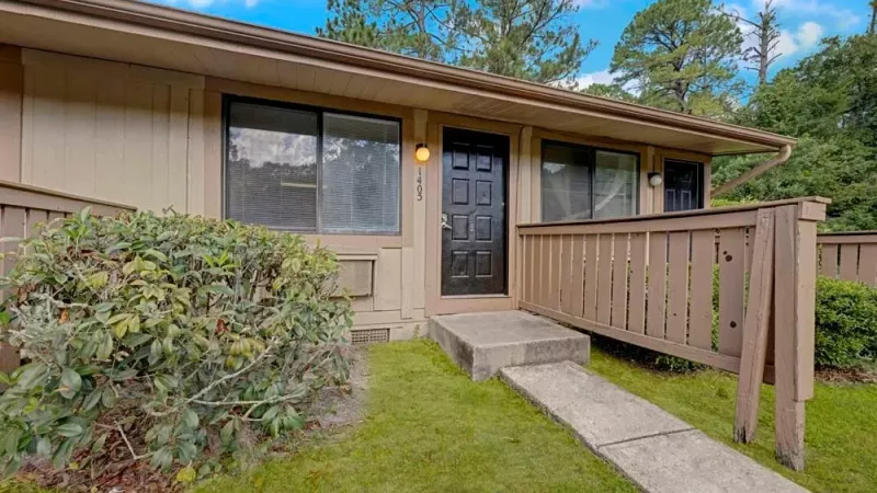A single-story apartment unit with a private fenced entrance and landscaped shrubs.