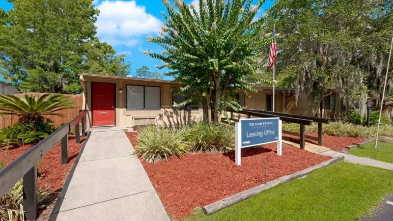 A leasing office with a red door, surrounded by manicured landscaping and a sign for Pelican Pointe.