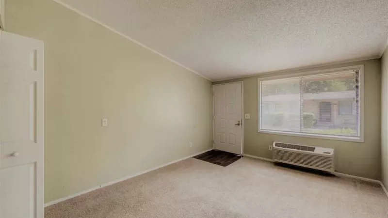 A bright living room with a large front window and a view of the outside greenery.