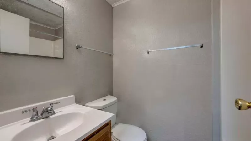 A clean bathroom with a simple sink, mirror, and a toilet under bright lighting.