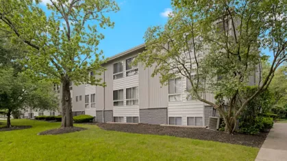 Exterior view of the apartment complex with landscaped greenery and tall trees.