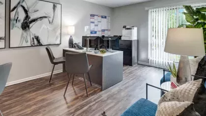 Bright leasing office with a desk, blue seating area, and a large window with blinds.