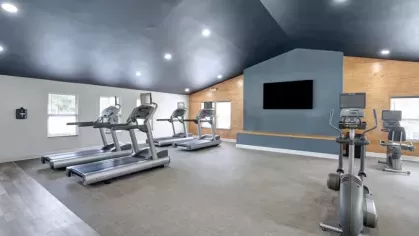 A spacious gym with several treadmills and exercise bikes under a vaulted ceiling.