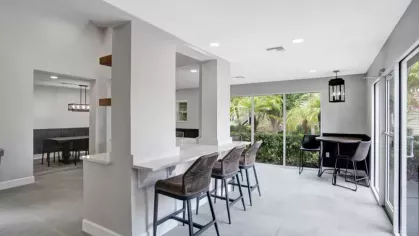 A bright cafe-style seating area with bar stools and views of greenery through large windows.