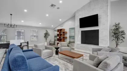 A modern living room with blue and gray furniture, a marble fireplace, and a mounted TV in a bright, open space.
