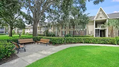 A landscaped courtyard with shaded seating, lush greenery, and residential buildings in the background.