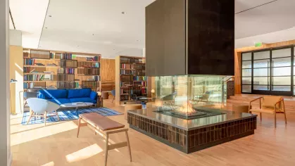 An inviting common area with a glass-encased central fireplace, ample seating, and an outdoor view, blending luxury and comfort for social gatherings.