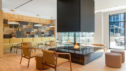 An inviting common area with a glass-encased central fireplace, ample seating, and an outdoor view, blending luxury and comfort for social gatherings.