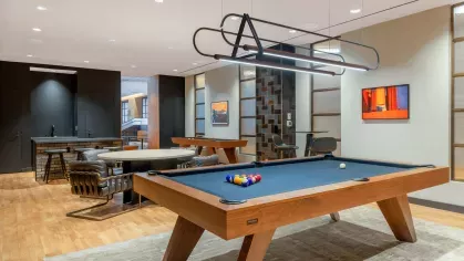A stylish game room at The Edmund Apartments, equipped with a pool table, shuffleboard, and contemporary seating areas for entertainment and socializing.