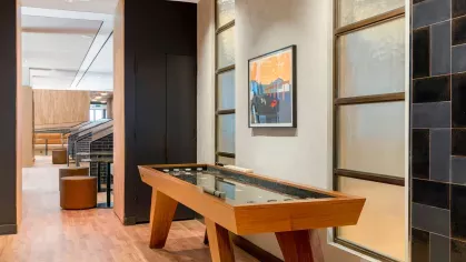 A stylish game room at The Edmund Apartments, equipped with a pool table, shuffleboard, and contemporary seating areas for entertainment and socializing.