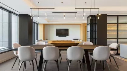 A modern library with wooden shelving filled with colorful books, two circular chairs, and a small round coffee table in a well-lit space with large windows.