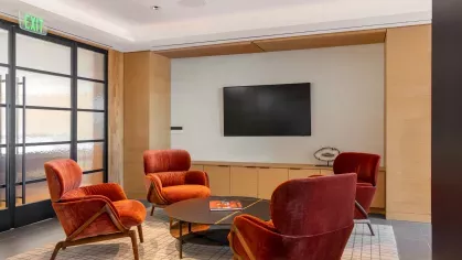 A spacious meeting room featuring a long wooden table with gray chairs, accent lighting, and built-in bookshelves for a professional yet inviting ambiance.