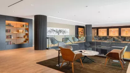 An open reading lounge with built-in bookshelves, orange leather banquettes, and modern furniture set against a wood-paneled backdrop.