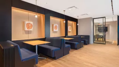 A stylish co-working area with long wooden tables, sleek chairs, and bookshelves, illuminated by modern pendant lights.