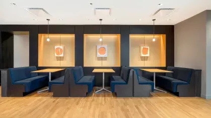A stylish co-working area with long wooden tables, sleek chairs, and bookshelves, illuminated by modern pendant lights.