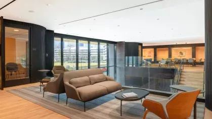 A stylish co-working area with long wooden tables, sleek chairs, and bookshelves, illuminated by modern pendant lights.