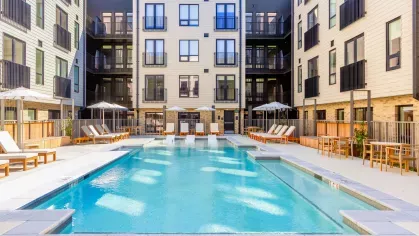 Outdoor pool area at The Edmund Apartments featuring lounge chairs, umbrellas, and in-pool seating surrounded by modern apartment buildings.