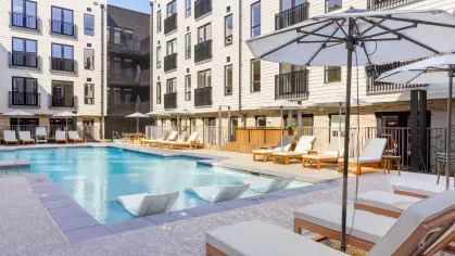 Outdoor pool area at The Edmund Apartments featuring lounge chairs, umbrellas, and in-pool seating surrounded by modern apartment buildings.