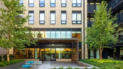 Fitness center exterior with modern glass windows, lush greenery, and vibrant outdoor seating.