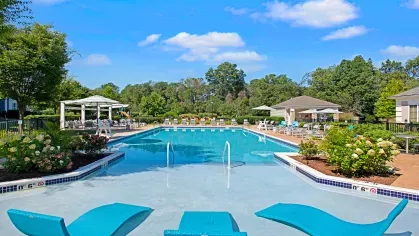 A sparkling outdoor swimming pool surrounded by lounge chairs, umbrellas, and lush landscaping at The Grove Somerset Apartments.