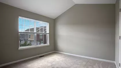 A bedroom with soft carpeted flooring, neutral wall colors, and large windows offering outdoor views of The Grove Somerset Apartments community.