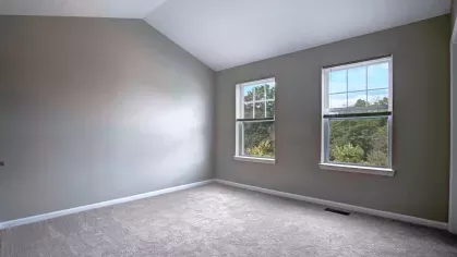 A bedroom with soft carpeted flooring, neutral wall colors, and large windows offering outdoor views of The Grove Somerset Apartments community.