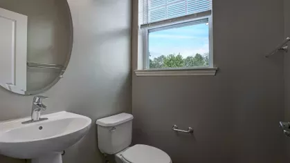 Modern bathroom with a pedestal sink, round mirror, and natural light streaming through a window.