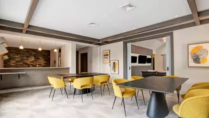 Sleek dining area featuring bold yellow chairs, dark tables, and an adjoining bar space.