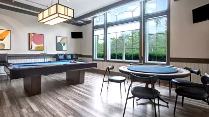 Modern game room with a pool table, poker table, and large windows providing natural light at The Grove Somerset Apartments.