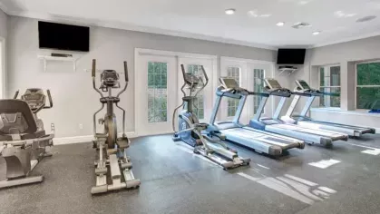 A well-equipped gym featuring treadmills, ellipticals, and large windows for natural light.