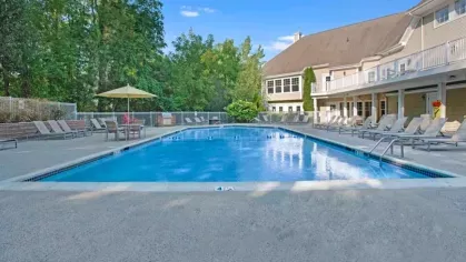 A close-up of an outdoor pool with a lounging area and building in the background on a sunny day.