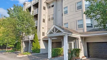 A beige multi-story apartment building with balconies and a landscaped entrance.