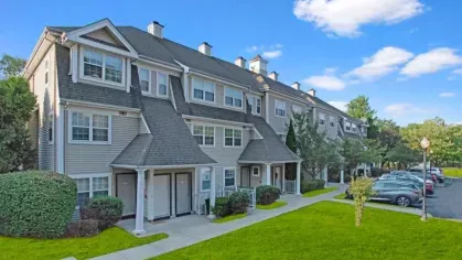A row of townhome-style buildings with green lawns and a sunny blue sky.