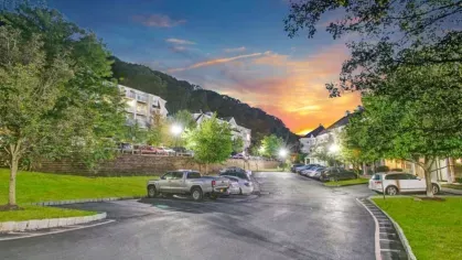 A parking lot in a residential complex during sunset, with well-lit buildings and trees.
