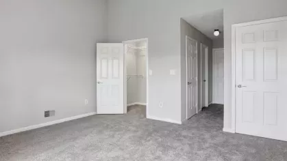 A master bedroom with plush carpet, a walk-in closet, and neutral-toned walls.