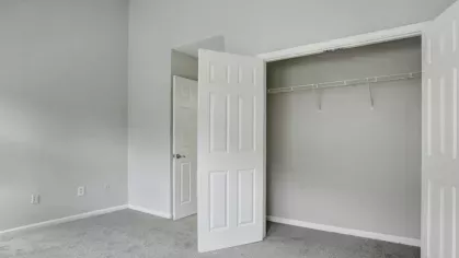 A bedroom with a simple closet, gray carpet, and neutral walls.