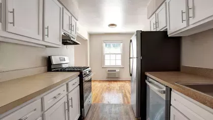 Modern galley kitchen with white cabinetry, stainless steel appliances, and natural light flowing in through a window, showcasing a cozy and functional layout.