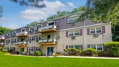 Exterior view of The Manors Apartments showcasing well-maintained green spaces, modern balconies, and a tree-lined backdrop.