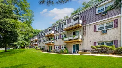 Exterior view of The Manors Apartments showcasing well-maintained green spaces, modern balconies, and a tree-lined backdrop.