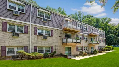 Exterior view of The Manors Apartments showcasing well-maintained green spaces, modern balconies, and a tree-lined backdrop.