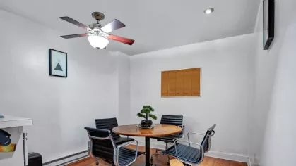 A spacious apartment at The Manors Apartments with a cozy dining space featuring hardwood floors and a contemporary ceiling fan.